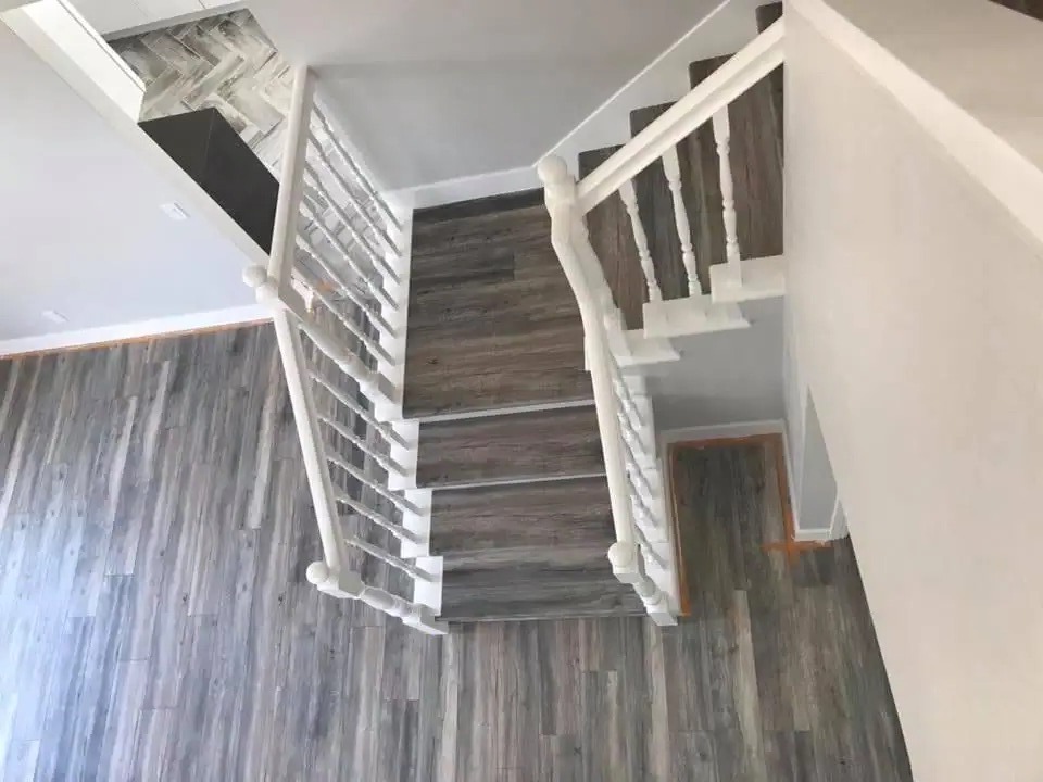 Staircase and landing covered in wood-look plank flooring with a white railing